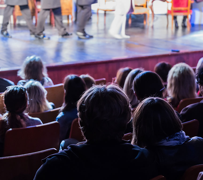 View of audience watching a play from the back of a theater